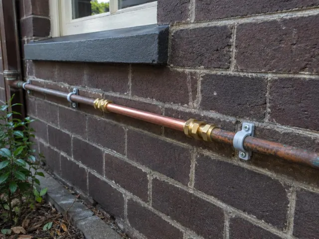 Repaired copper water pipe on a brick house wall beside a window in Petersham