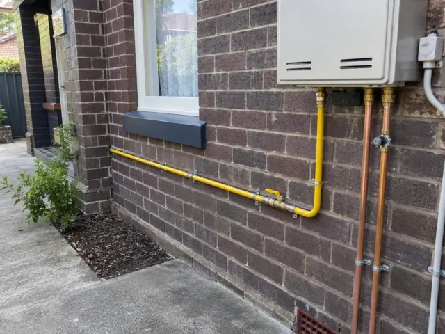 Yellow gas piping and fittings on a brick exterior wall beside a window in Lewisham