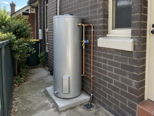 Outdoor hot water cylinder beside a brick wall and window with copper pipework in Summer Hill