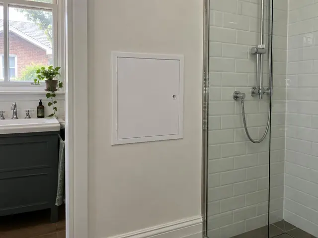 Bathroom wall with a small access panel beside a tiled shower and vanity in Summer Hill